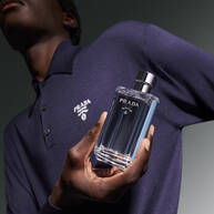 Torso of man in blue polo holding L'Homme Prada L'Eau Men's Eau de Toilette Spray