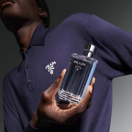 Torso of man in blue polo holding L'Homme Prada L'Eau Men's Eau de Toilette Spray
