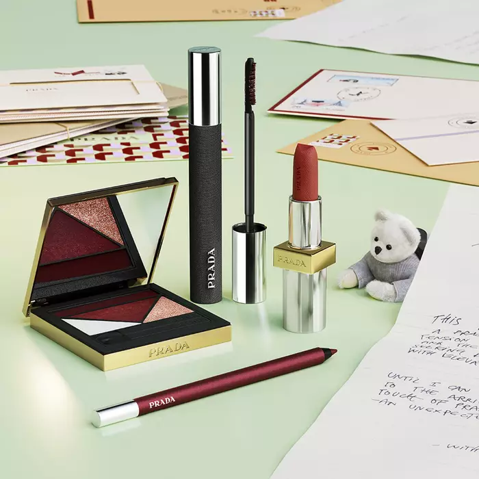Prada Holiday 2026 Mahogany collection with Lipstick, Mascara, Eye Palette, Eye Pencil, teddy bear and letters on a light green background