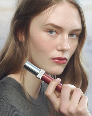 Prada Summer Stories Caucasian Model with Reflection Lip Gloss in hand on a muted beach background