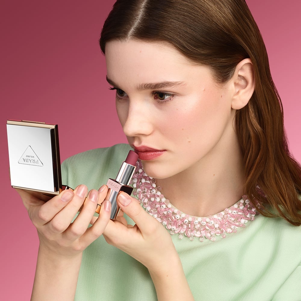 Verlee (blonde model) is wearing Prada Light Glowing Lipcolor Rosewood and Glowing Powder Champagne on a pink background.