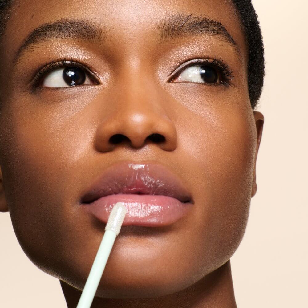 Model with deep skin tone applying the Prada Reflection Glossy Liquid Balm in the Universal shade.